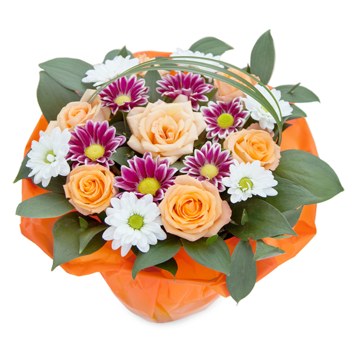 Overflowing with vibrancy and local charm, this top-down composition showcases a thoughtfully arranged bouquet capturing the warmth of Old Oak Common. The focal point is a clustering of generously petaled roses in hues from gentle peach to luminous orange, each bloom unfurling to display its soft velvety richness. Embedded amongst these are crisp white chrysanthemums, their delicately arching petals surrounding lime-green centers, paired with dramatic purple-mauve chrysanthemums whose intricate petals surround bright yellow-green hearts, conjuring the wildflower borders seen along the Grand Union Canal. Glossy, broad-leafed foliage curves gently between the blossoms, providing a deep green stage that amplifies the bouquet's sunset palette. Rising above, a refined loop of bear grass arches over the arrangement, mirroring the graceful tracks weaving through Old Oak Common's historic railway yards. The entire structure is wrapped at the base in cheerful orange cellophane - its crinkle and translucence picking up the community's energy and the gathering joy of local celebrations. This floral design, ideal for expressing appreciation, marking special occasions, or simply sharing a touch of natural artistry, highlights Flower Delivery Old Oak Common's commitment to beauty and attentive craftsmanship for every neighbour across the area.